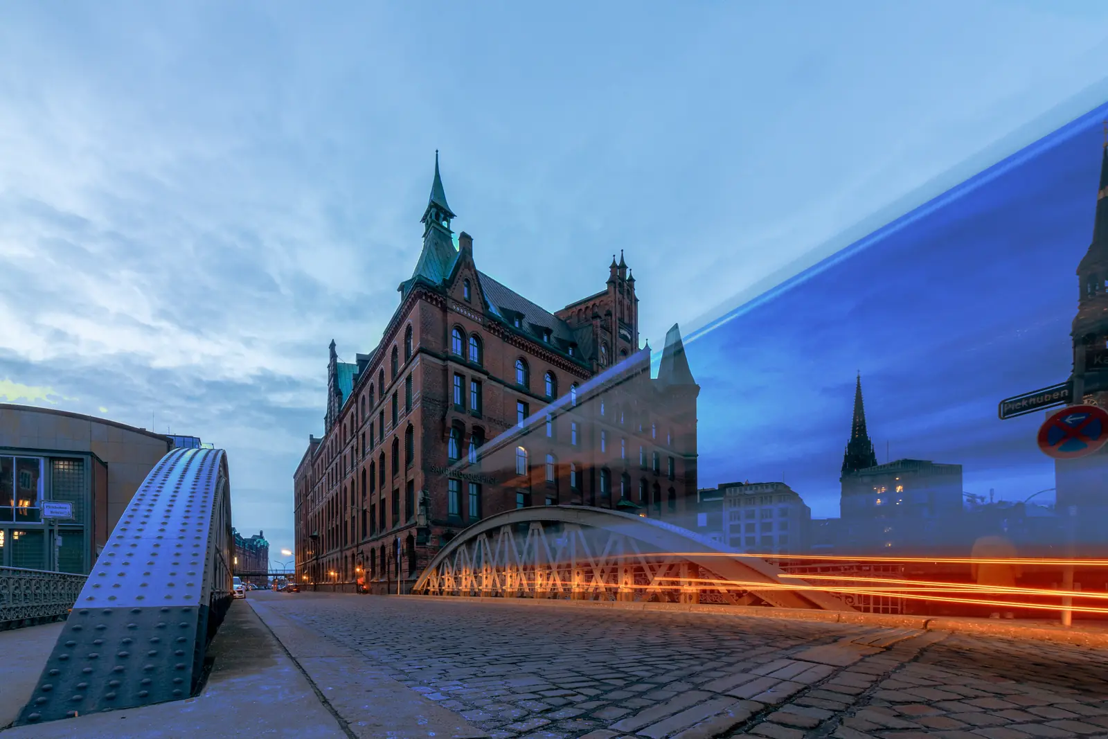 Sandtorquaihof in der Hamburger Speicherstadt zur blauen Stunde mit Lichtspur einer vorbeifahrenden Bahn