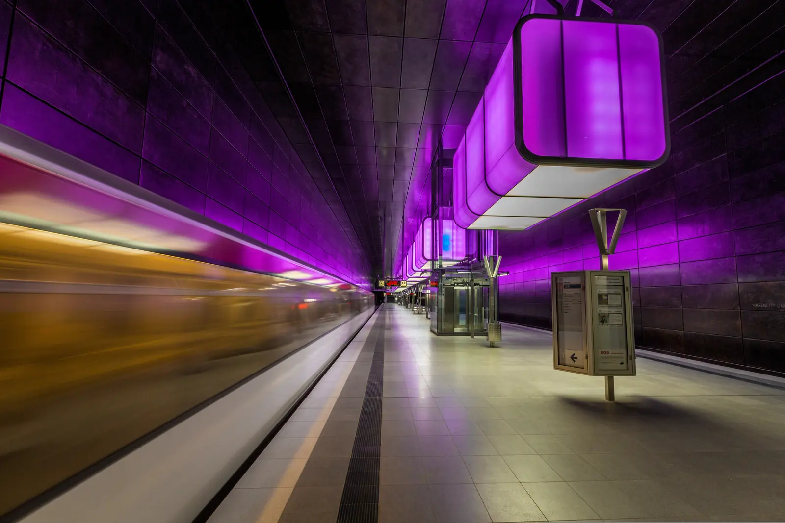 U-Bahn-Station HafenCity Universit&auml;t in Hamburg mit violetter Beleuchtung und einfahrender Bahn